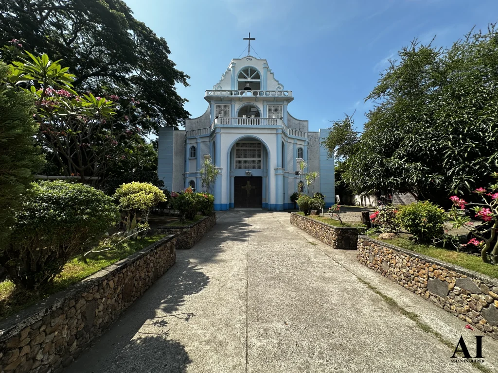 Exterior view of the St. Nicholas of Bari Parish in Siaton, Negros Oriental, featuring its unique sky-blue and white tiered facade and stone-lined garden path under a clear blue sky.