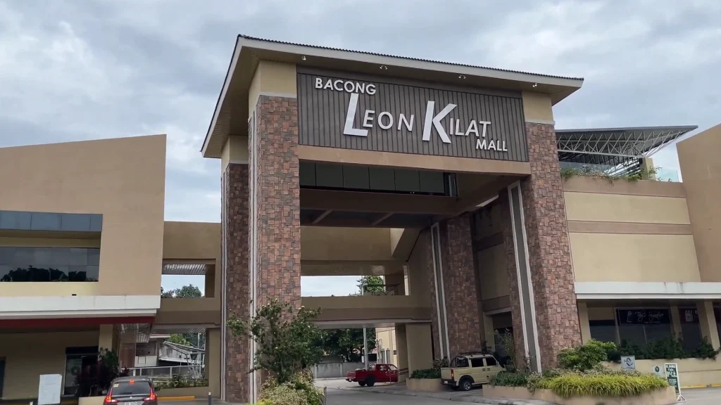 Wide-angle shot of the Bacong Leon Kilat Mall entrance under an overcast sky, featuring modern stone-cladded pillars and a minimalist architectural design with very little traffic.