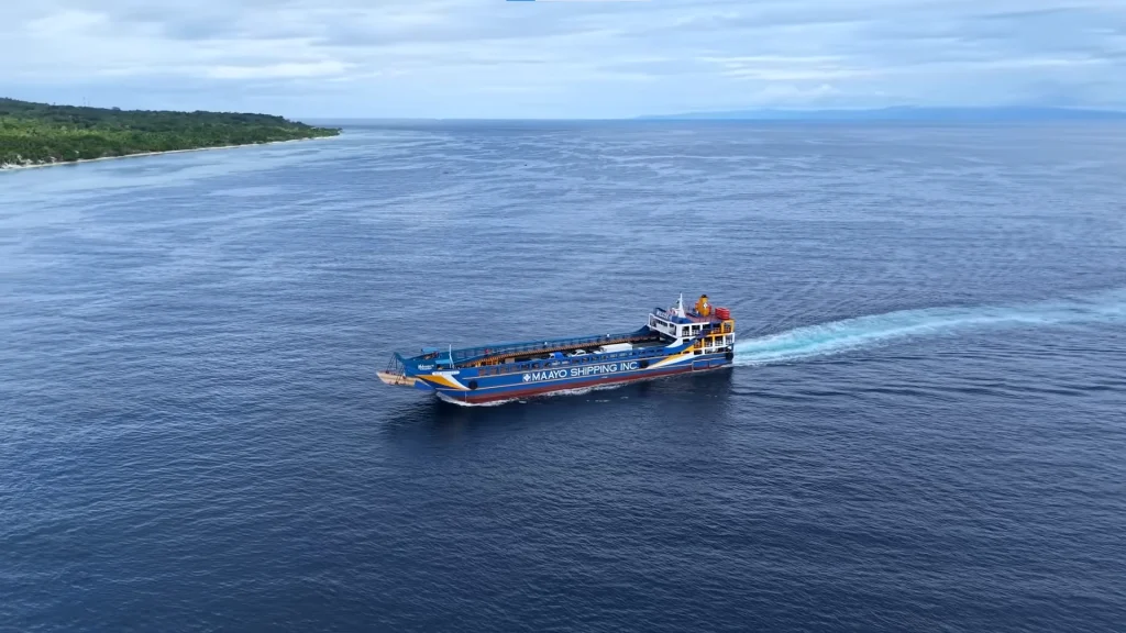 Aerial drone view of a Maayo Shipping Ro-Ro barge cruising across the deep blue waters of the Tañon Strait, with the green coastline of Sibulan, Negros Oriental, visible in the background.