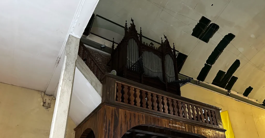 The Zaragoza Pipe Organ inside Bacong Church is mounted above a wooden choir loft with carved railings, dark organ pipes, Gothic-style wooden details, and an aged church ceiling visible above.