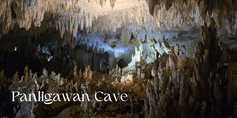 Featured image of Panligawan Cave showing a large underground chamber filled with dense stalactites hanging from the ceiling, rugged stalagmites rising from the cave floor, and illuminated limestone formations.